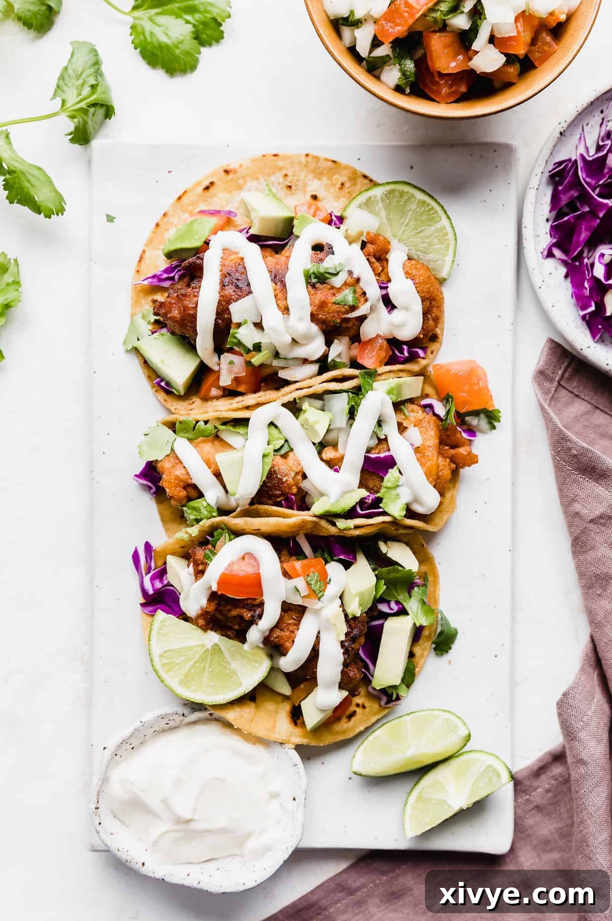 Three Baja Fish Tacos on a white plate with white sauce overtop. 