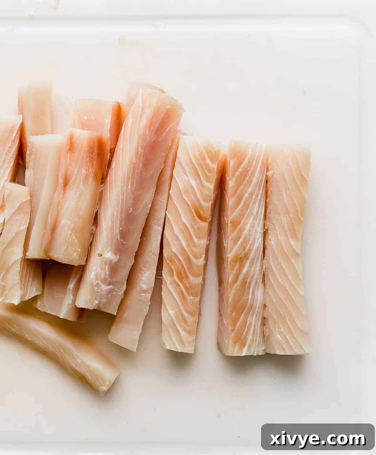 Mahi Mahi fish sliced into thin strips which are resting on a white cutting board.