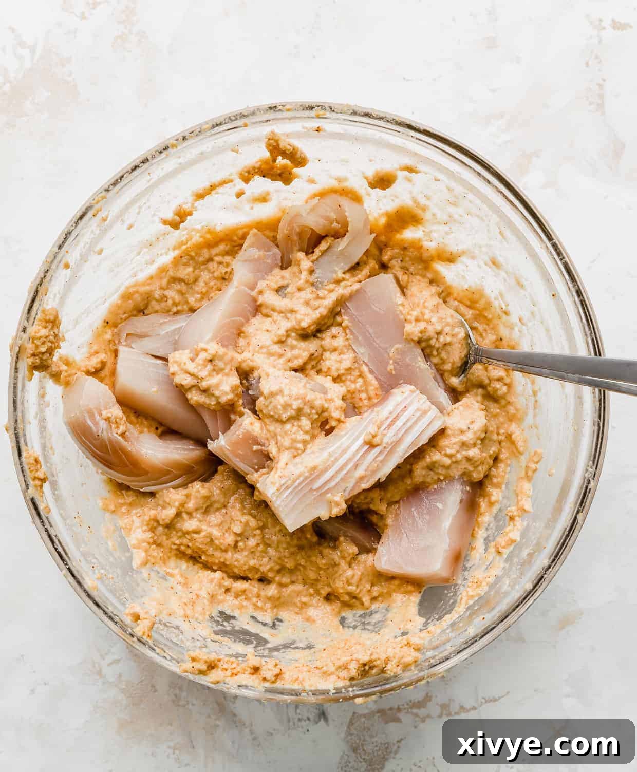 Strips of Mahi Mahi being stirred into a batter, in a glass bowl.