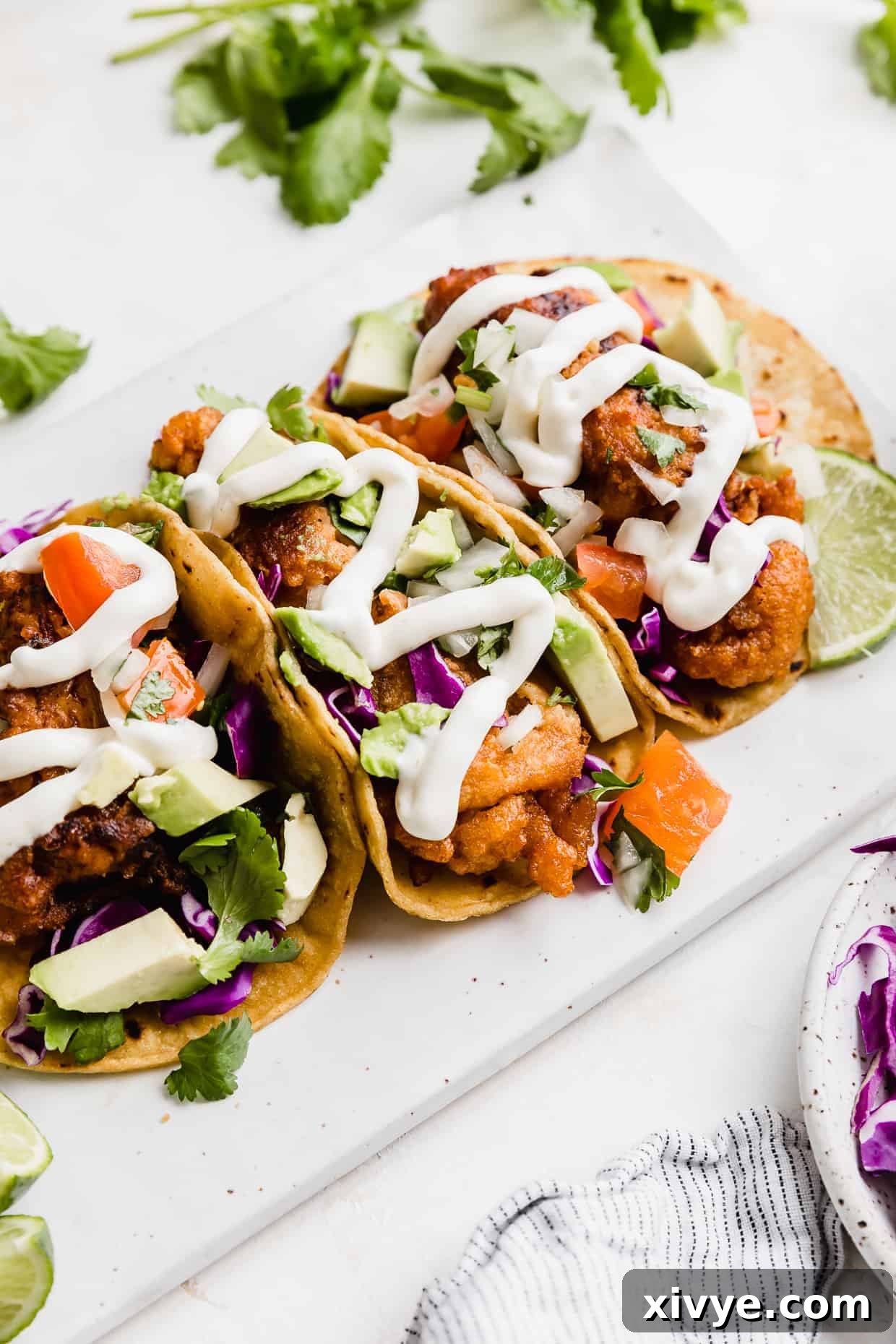Baja Fish Tacos on a white plate topped with white sauce, pico de Gallo, avocado, and cabbage. 