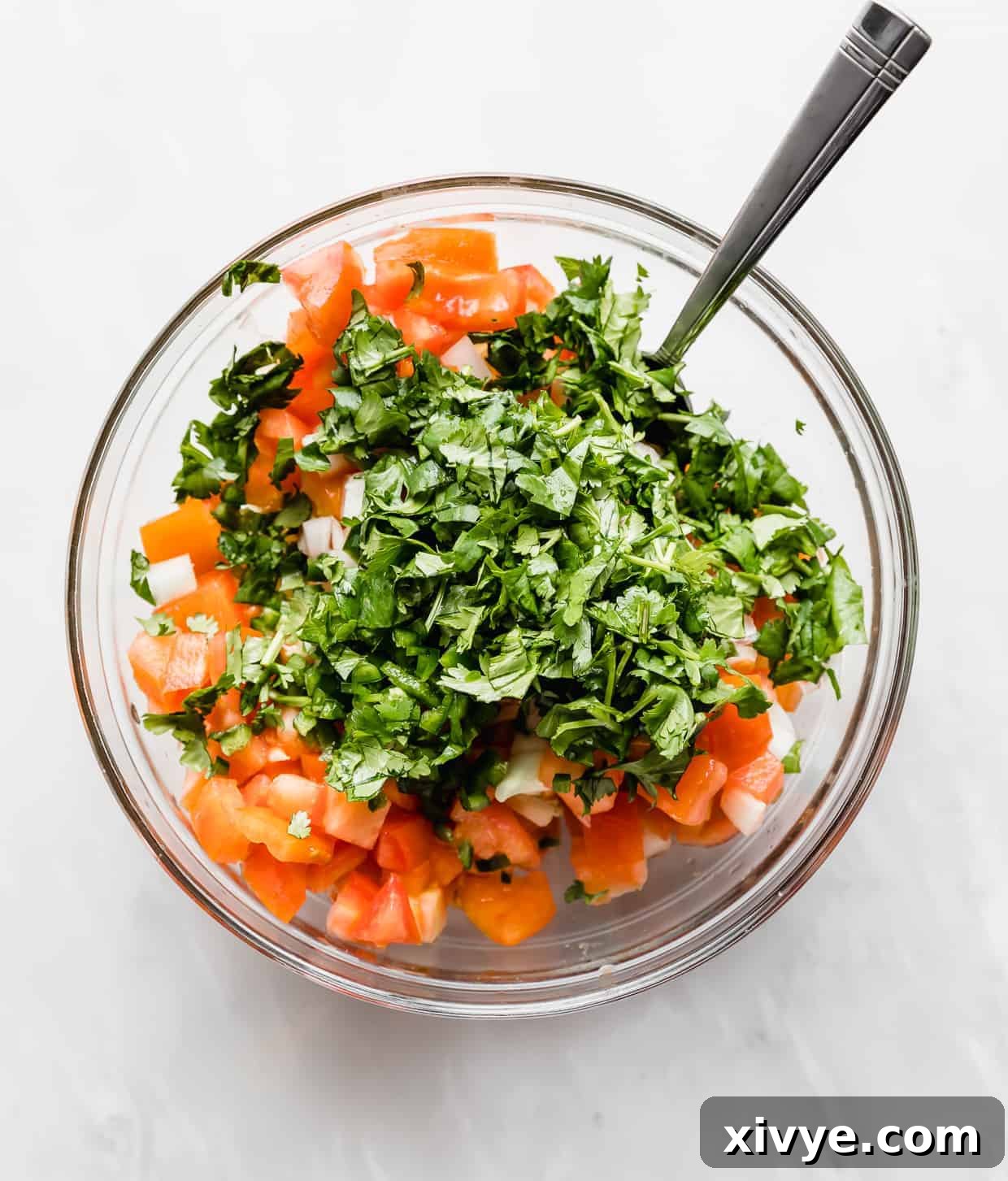 A glass bowl full of diced onion, tomato, and chopped cilantro.