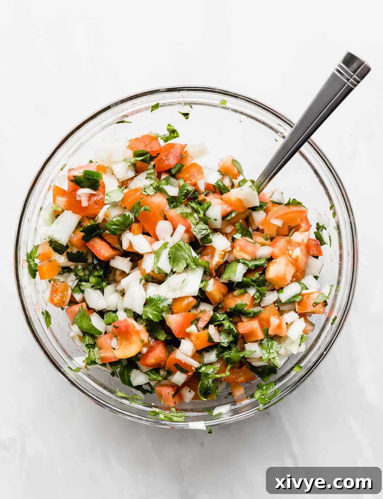 A glass bowl full of fresh Pico de Gallo against a white background.