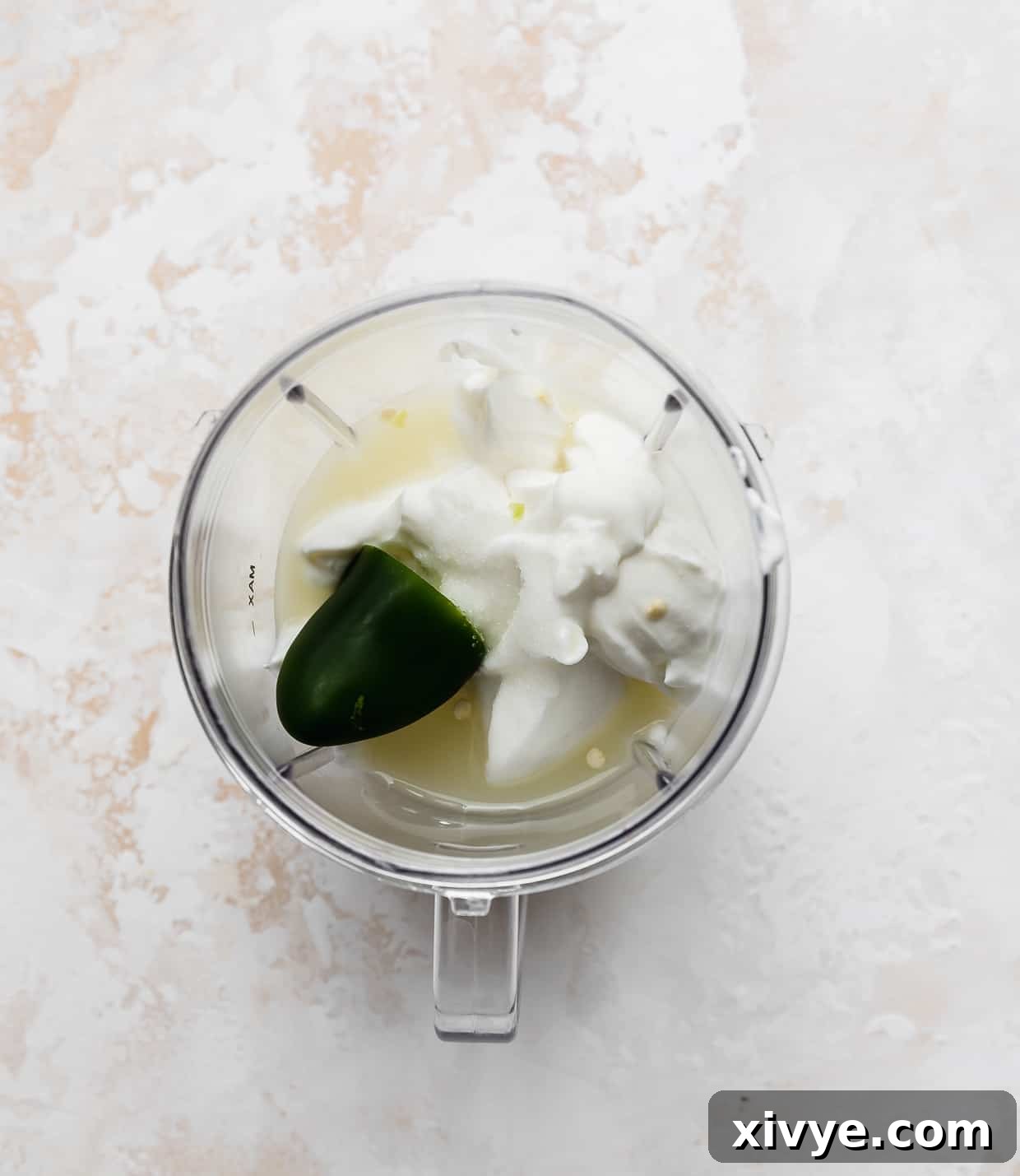 A small blender with white yogurt, half of a jalapeño, and lime juice in it. 