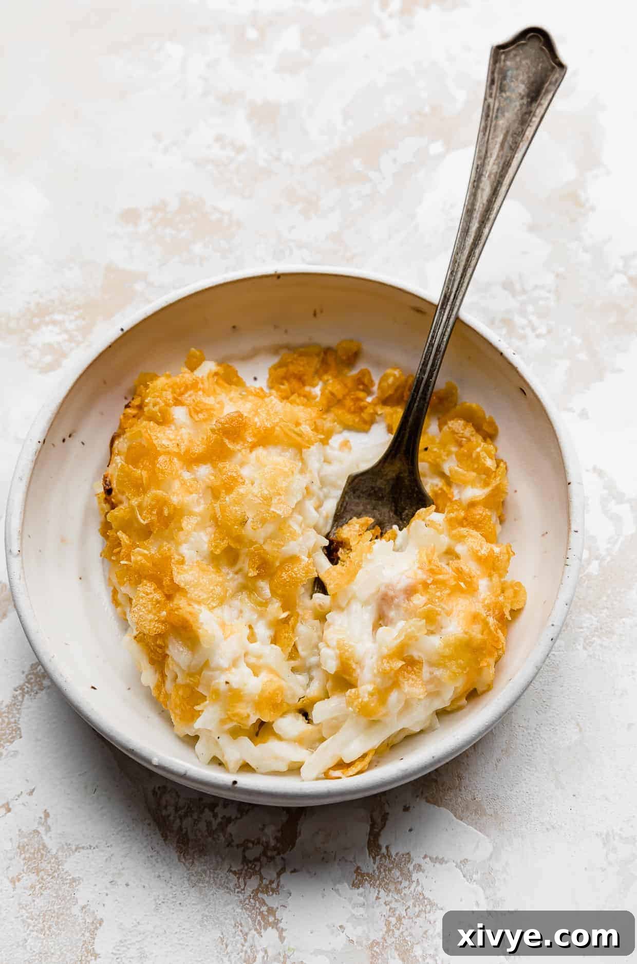 Golden Comfort Bake 2 A serving of golden-brown Funeral Potatoes on a white plate with a fork, ready to be enjoyed.