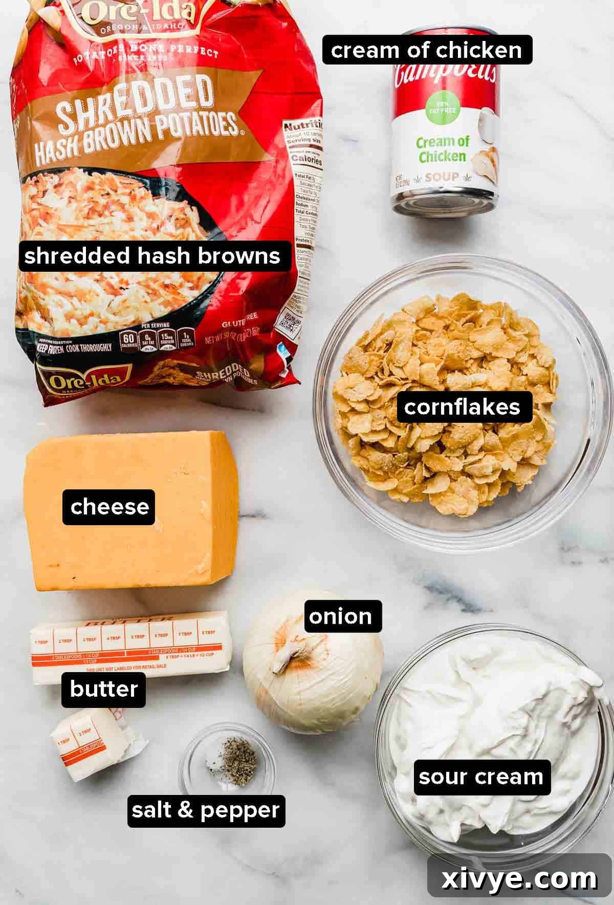 Golden Comfort Bake 3 Ingredients for Funeral Potatoes laid out on a white background: frozen shredded hash browns, block of cheddar, cornflakes, butter, diced onion, and a can of cream of chicken soup.