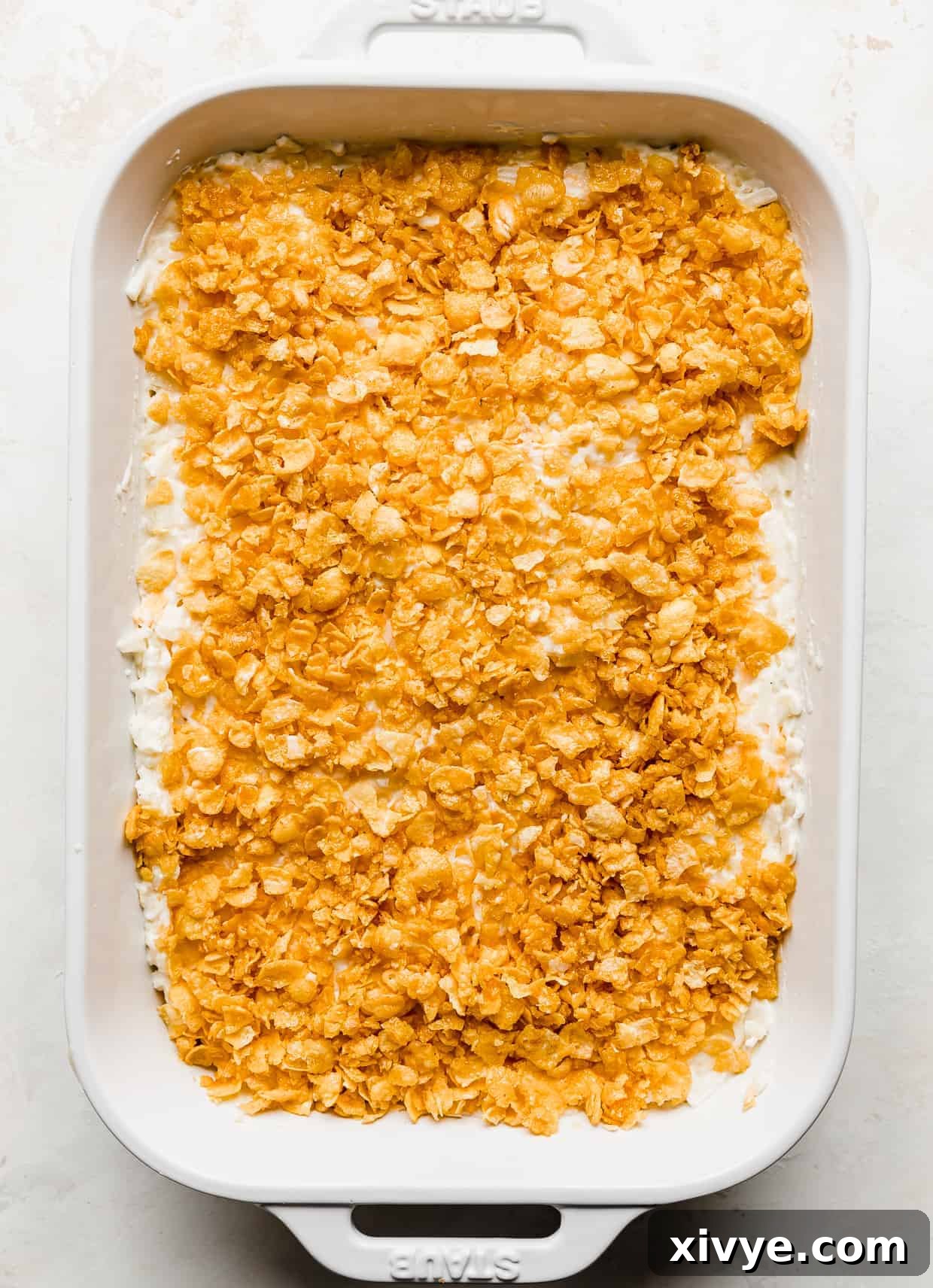 Golden Comfort Bake 8 An unbaked Funeral Potato casserole in a white dish, beautifully topped with crushed cornflakes, waiting to be baked.