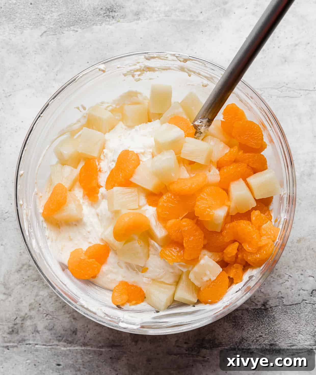 Canned and drained mandarin oranges and pineapple chunks atop a yellow cream colored pudding mixture.