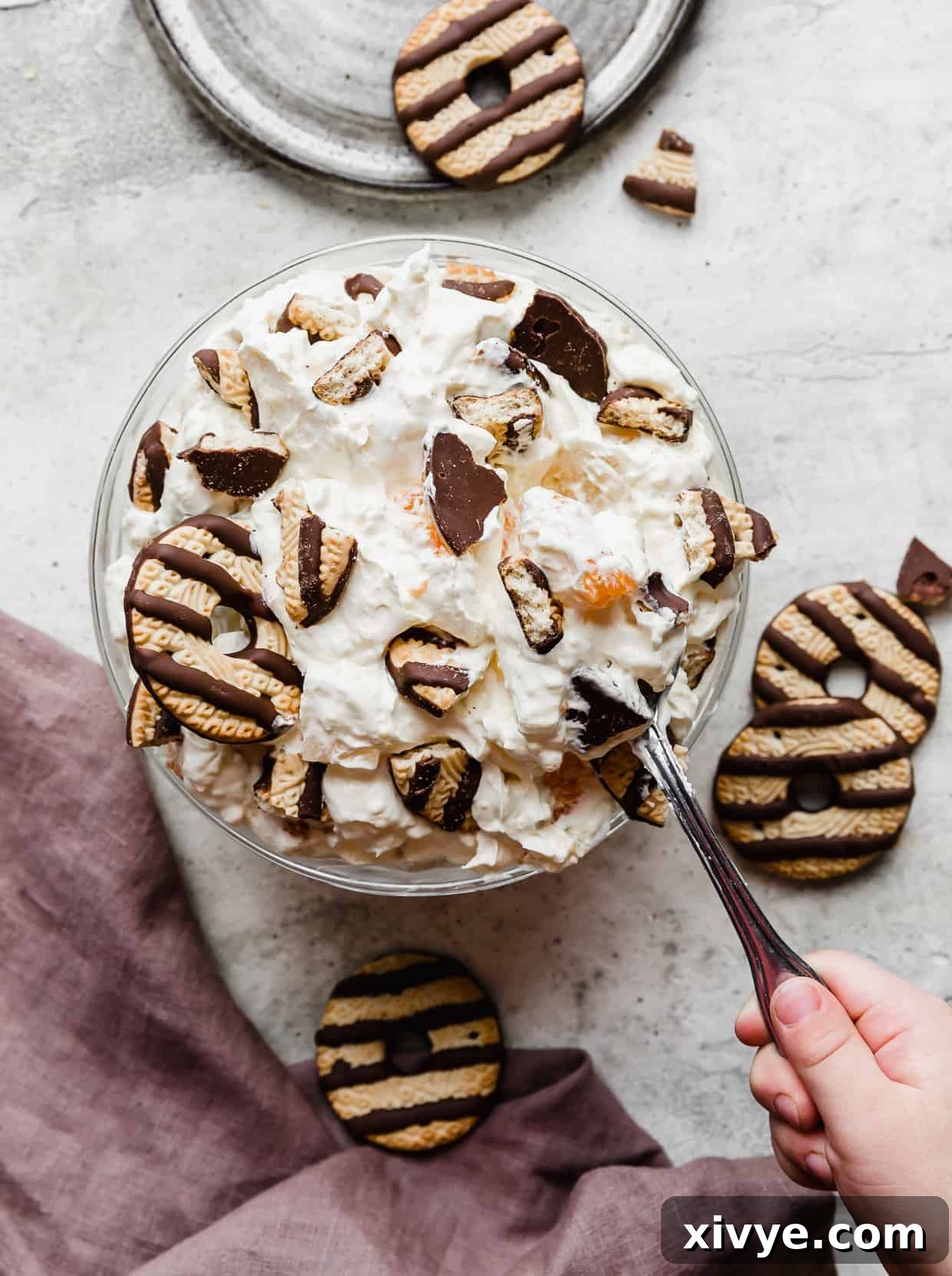A hand holding a spoon scooping out some cookie salad from a large bowl.