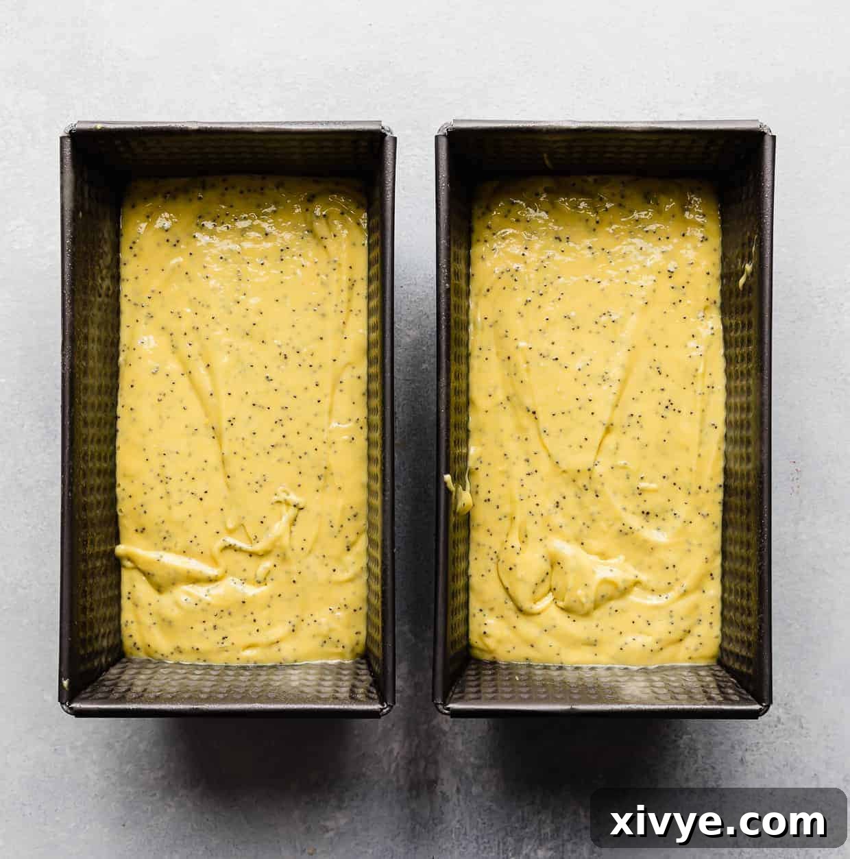 Two loaf pans, one 8x4-inch and one 8x5-inch, brimming with golden-yellow lemon poppy seed bread batter, perfectly smooth and ready to be placed into the oven for baking.