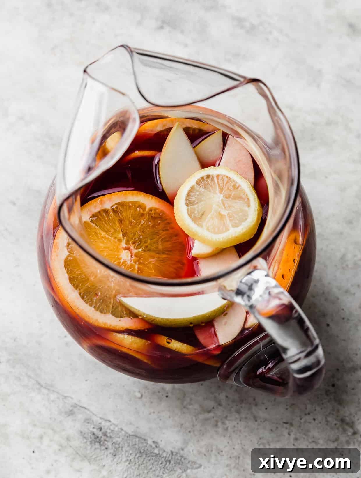 Virgin Sangria 4 A virgin sangria drink in a glass pitcher with slices of fresh oranges, apples, lemons, and pears floating in the drink.