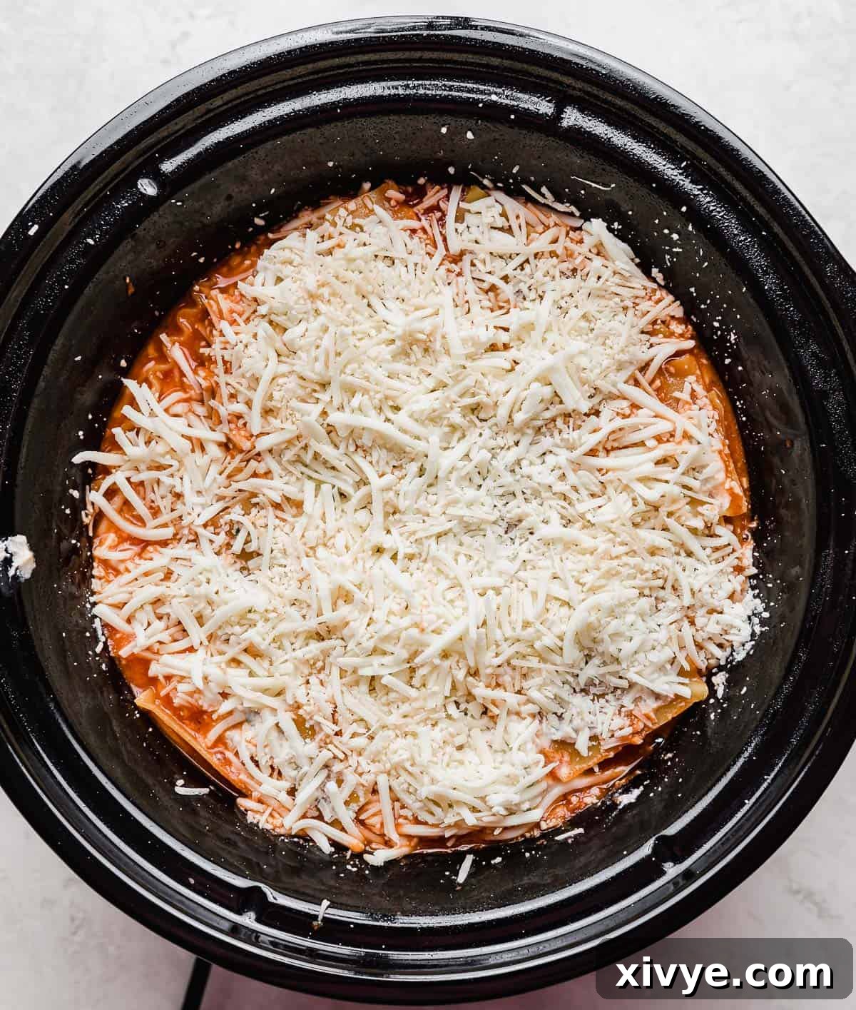 Shredded mozzarella cheese overtop Slow Cooker Lasagna in a round crockpot.
