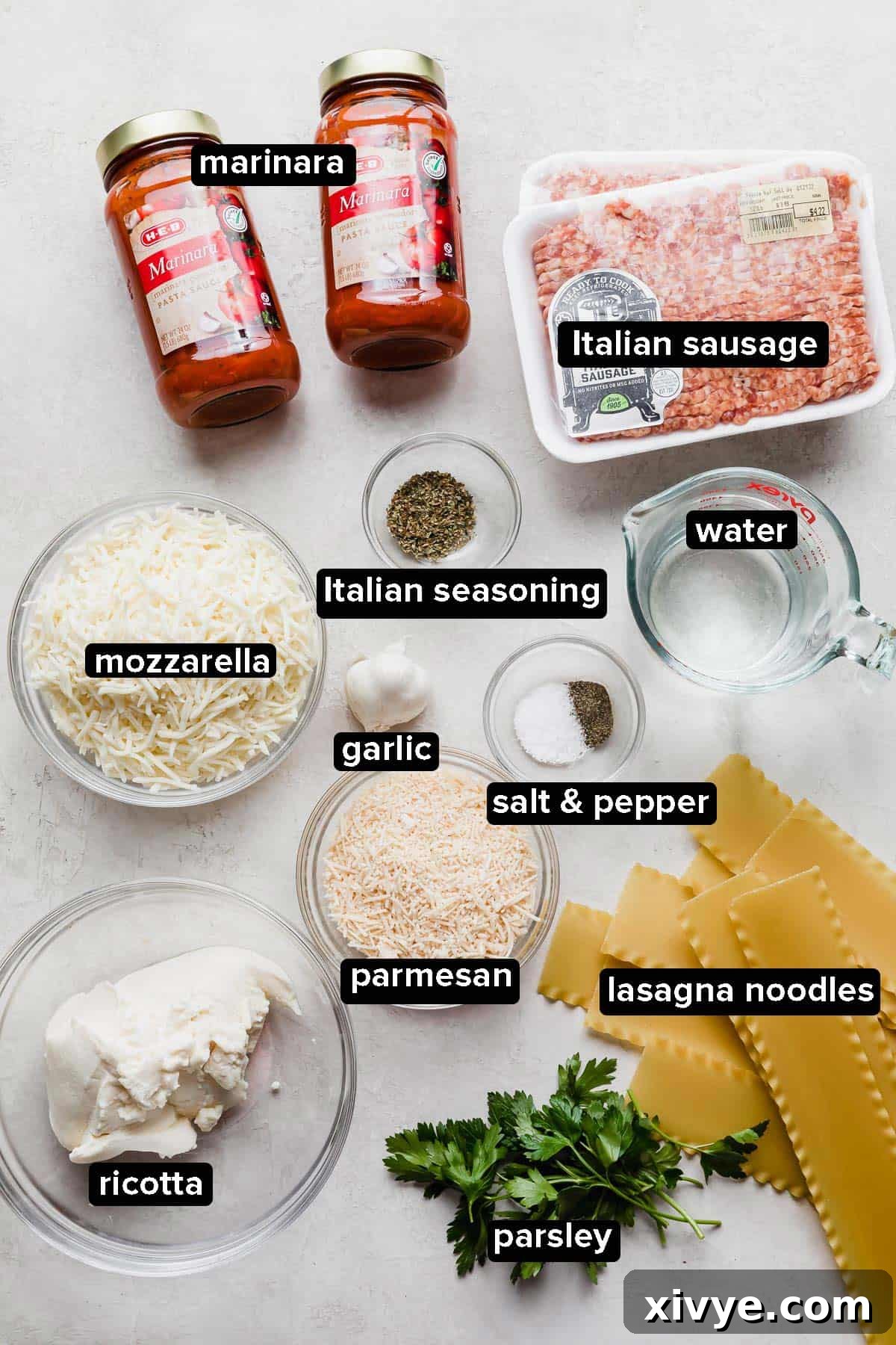 Slow Cooker Lasagna ingredients on a white background including jar sauce, ricotta, and uncooked lasagna noodles.