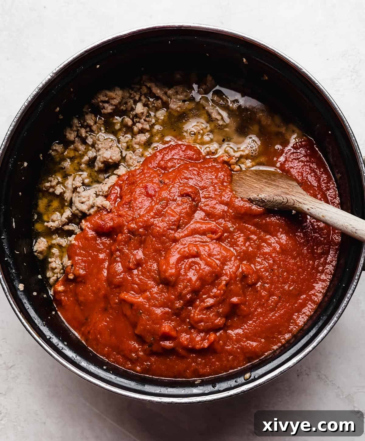 A pot with ground sausage and red marinara sauce in it.