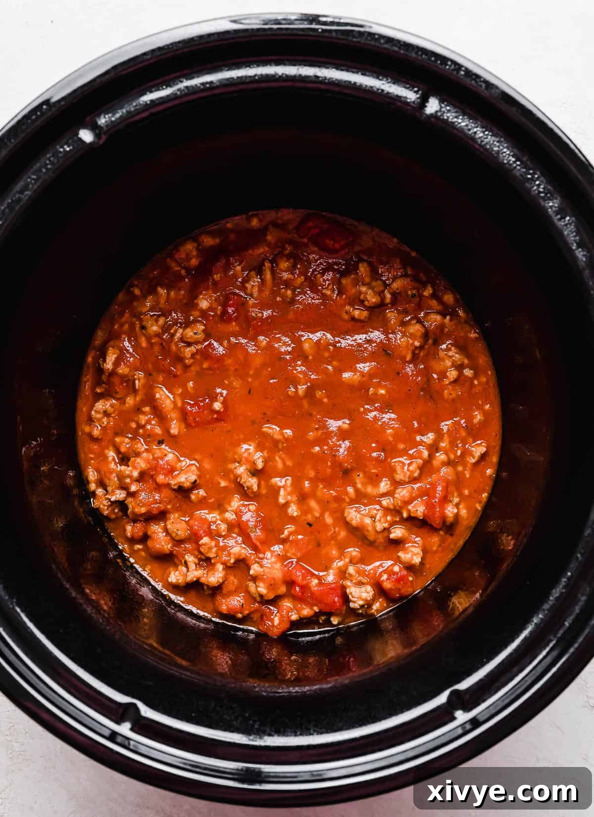 A round black crock pot with ground meat and red sauce in it.