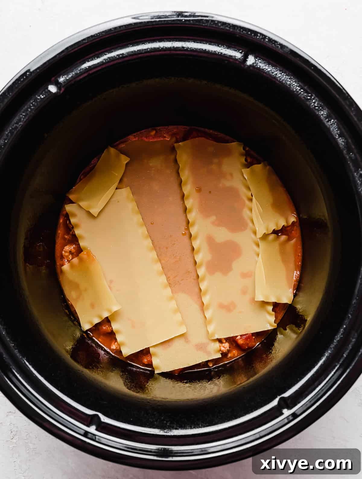 Lasagna noodles in the base of a black round slow cooker.