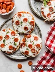 Three English muffin pizzas topped with mini pepperoni's on a gray plate.
