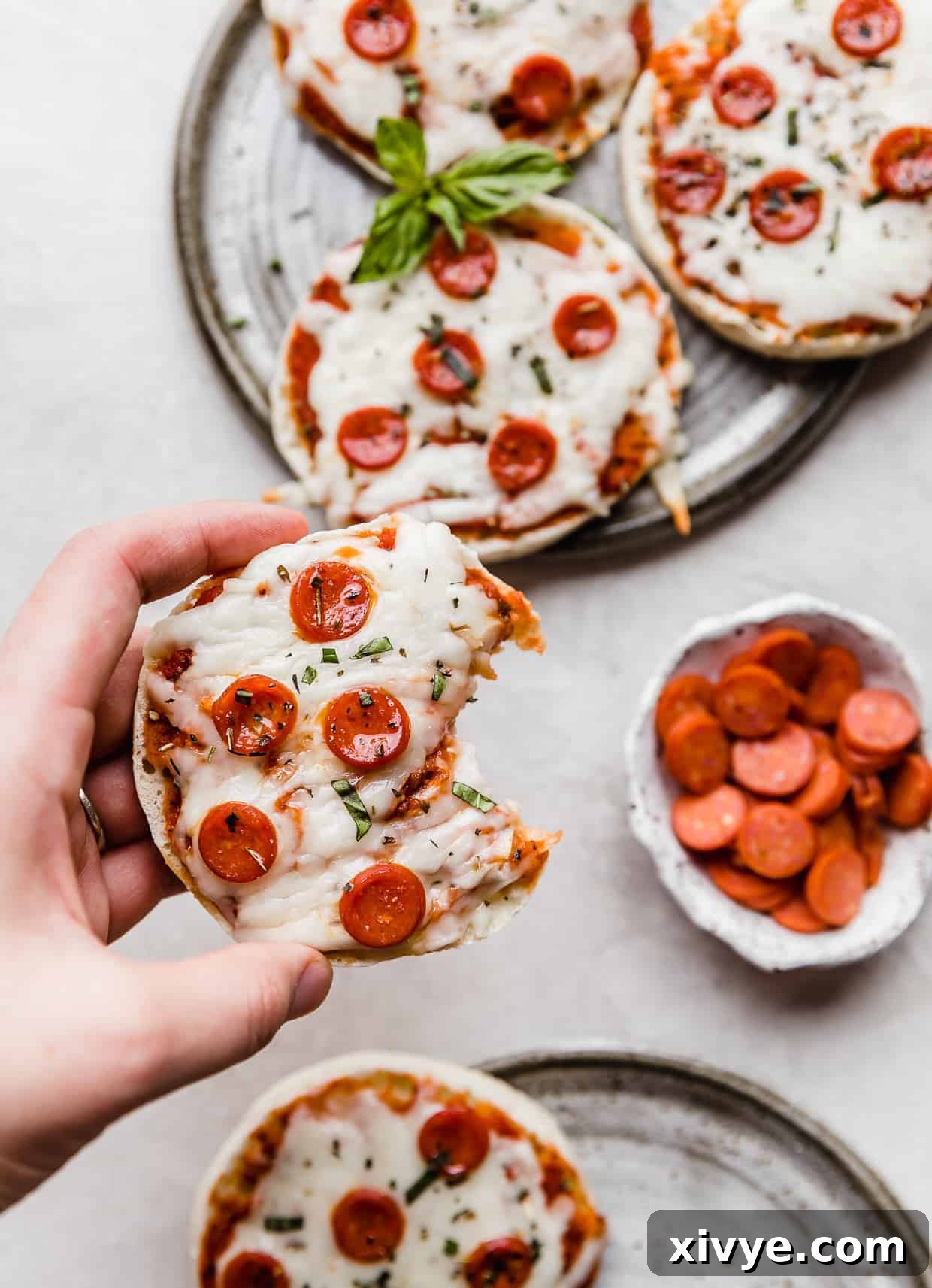 A hand holding an English muffin pizzas with a bite taken out of it. 