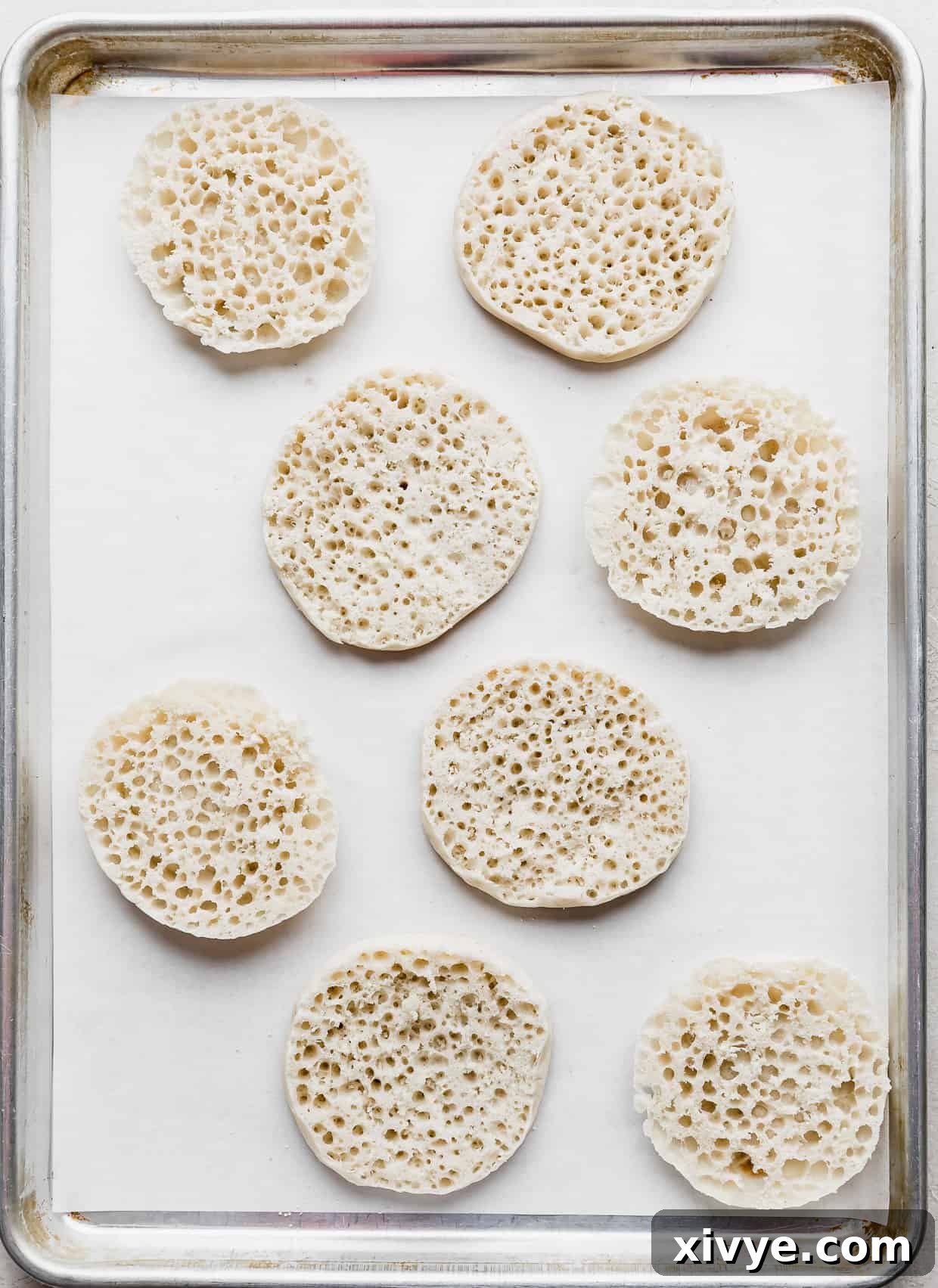 8 English muffins halves on a parchment lined baking sheet, ready for toppings.
