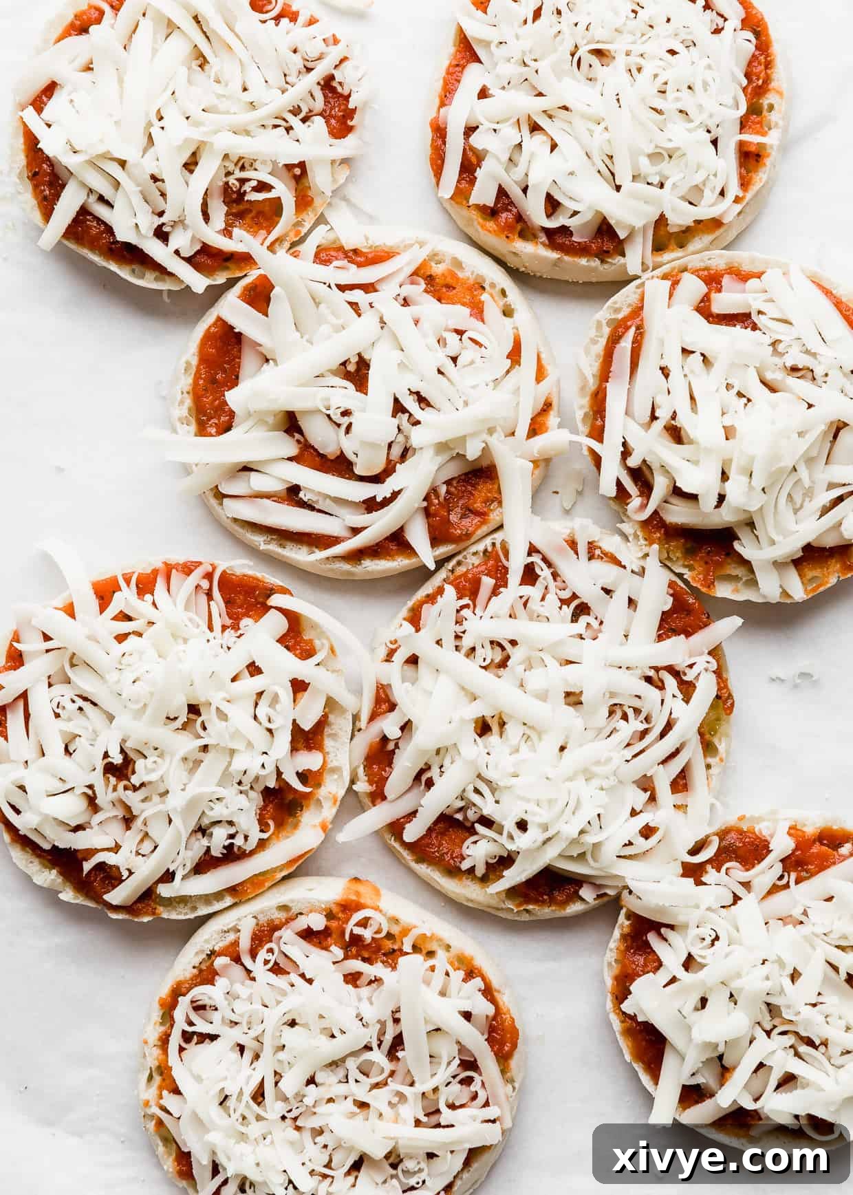 Shredded mozzarella overtop of eight English muffin halves, perfectly coated.
