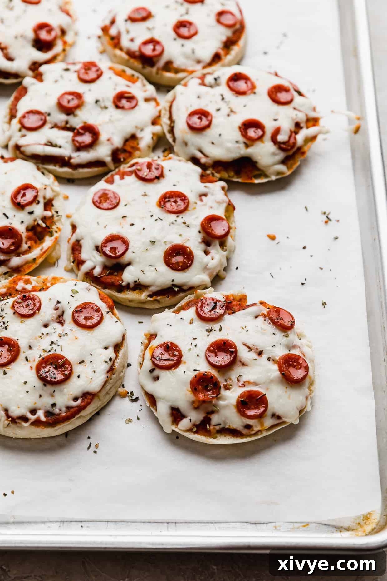 Baked English Muffin Pizzas topped with mini pepperonis on a white parchment lined baking sheet, golden and delicious.