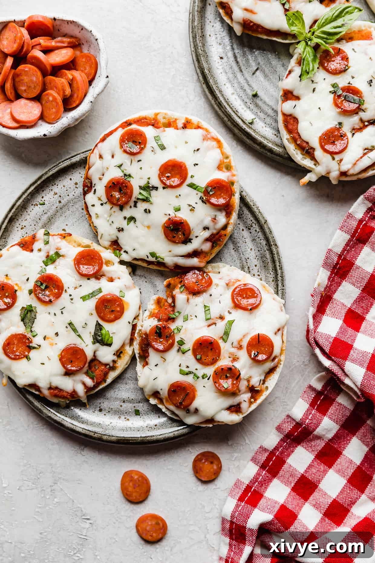 Three English muffin pizzas topped with mini pepperoni's on a gray plate, showcasing the delicious result.