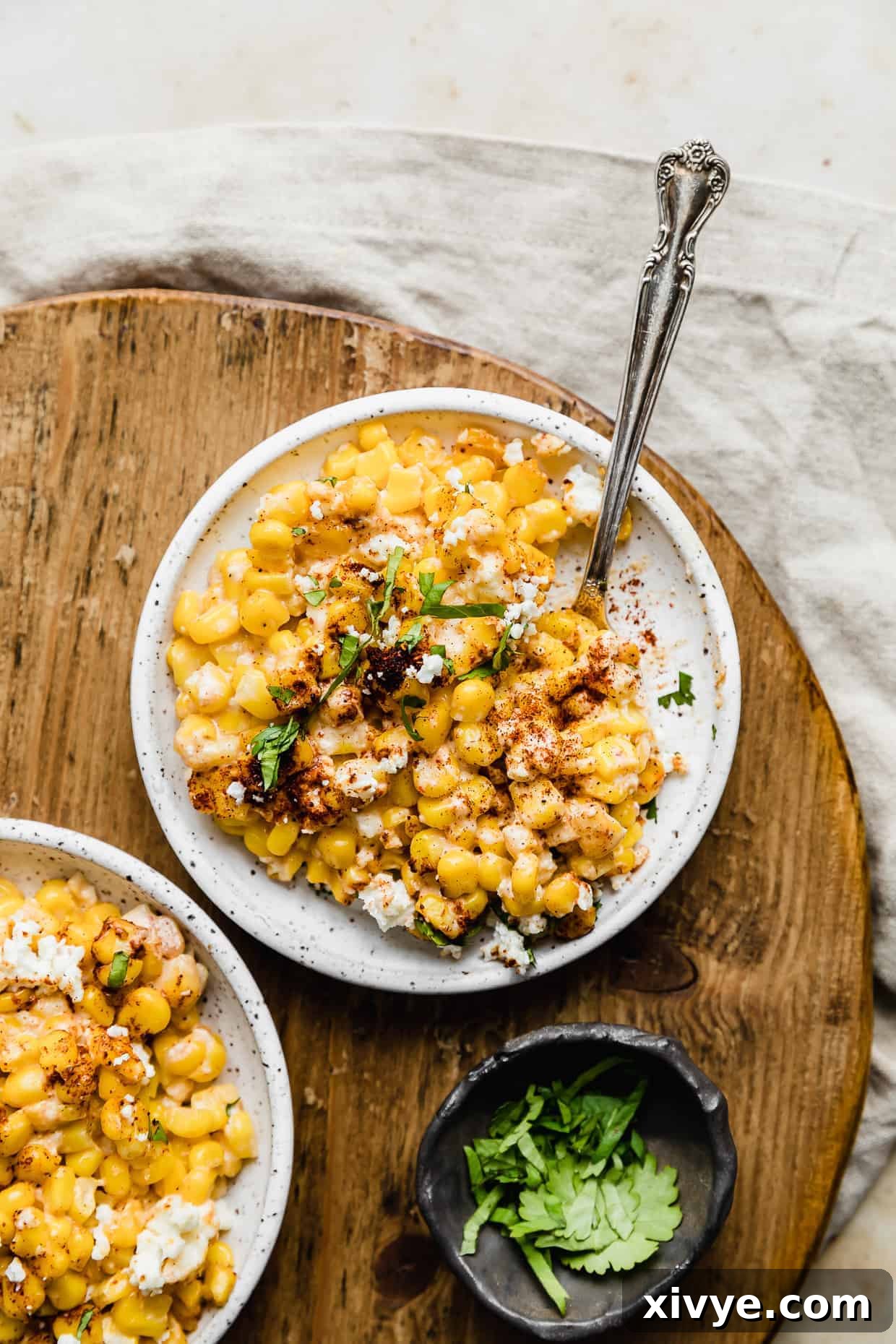 A white bowl with Mexican Street Corn Casserole in it, resting on a round wooden board. 