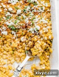 A large serving spoon scooping out Mexican Street Corn Casserole from a white baking dish.