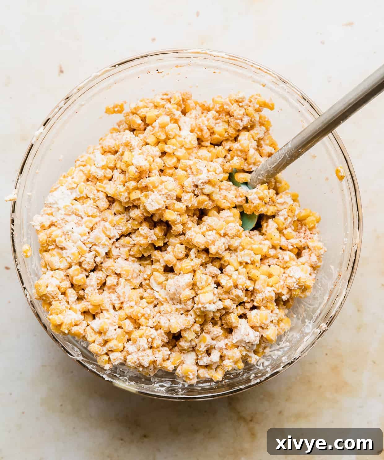 Mayo and sour cream covered corn kernels in a large glass bowl.