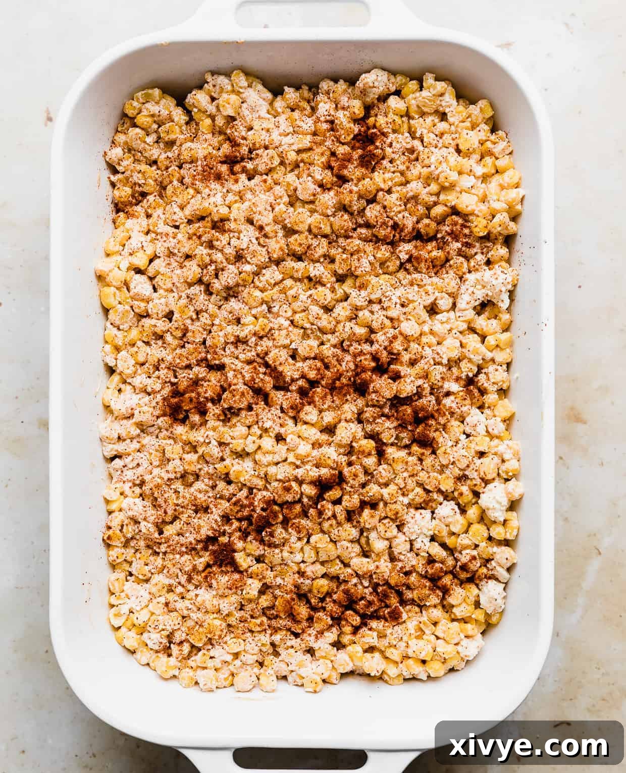 A white rectangular baking dish full of Mexican Street Corn Casserole that has been sprinkled with chili powder.