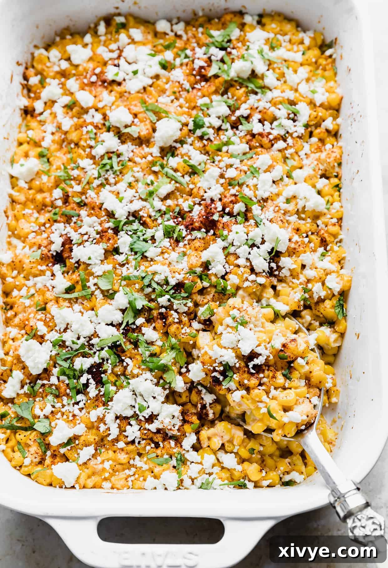 A spoon scooping into a casserole dish that is full of cilantro and chili powder covered corn kernels. 