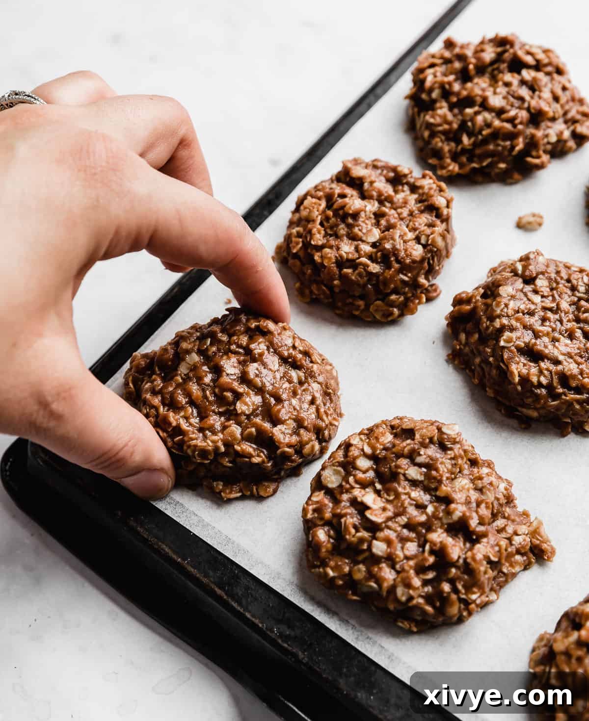 A hand gently picking up a delectable Chocolate Peanut Butter No Bake Cookie from white parchment paper, ready to be eaten.
