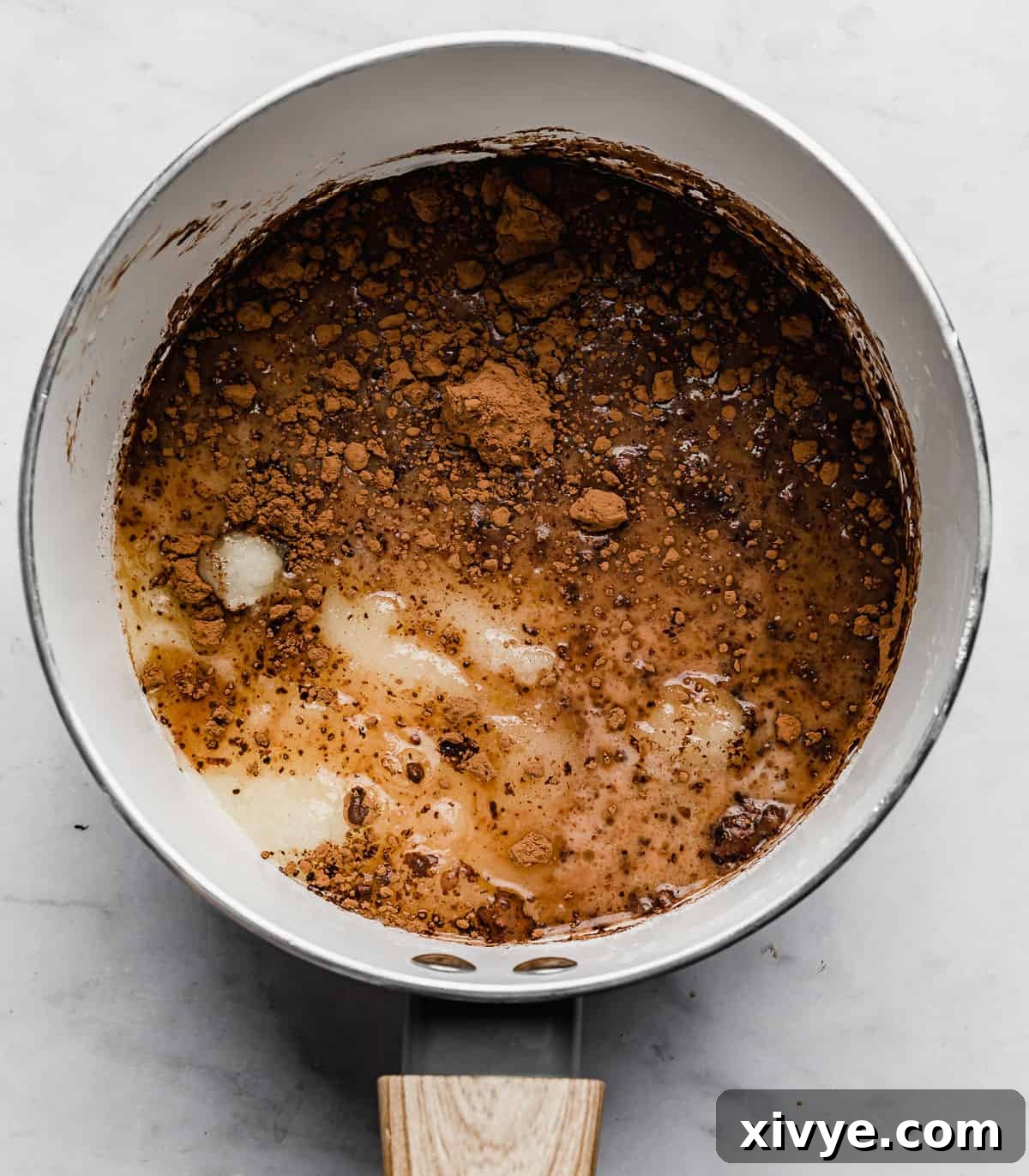 A white pot filled with cocoa powder, milk, and sugar, a key step in making small batch no bake cookies.
