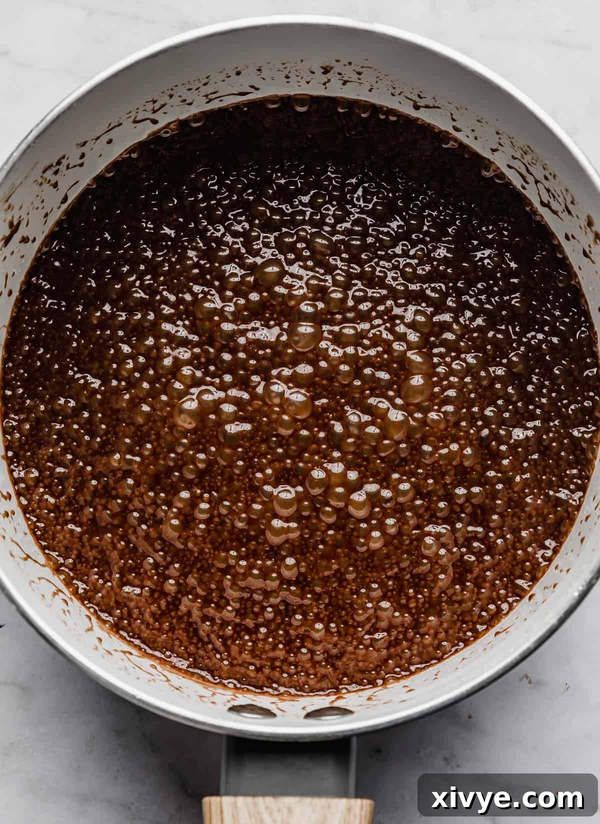 A liquid chocolate mixture, essential for making delicious chocolate peanut butter no bake cookies, boiling gently in a white pot.