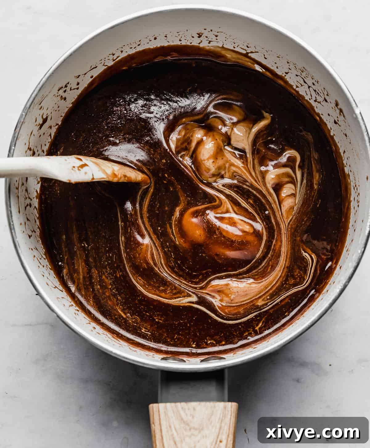 A spatula efficiently stirring creamy peanut butter into a rich chocolate mixture, creating a smooth blend.