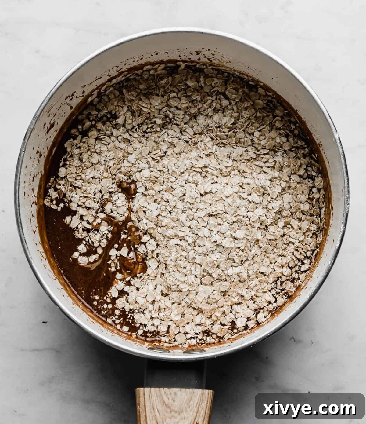 Quick oats being mixed into a rich chocolate peanut butter sauce within a white pot, for a no-bake cookie recipe.