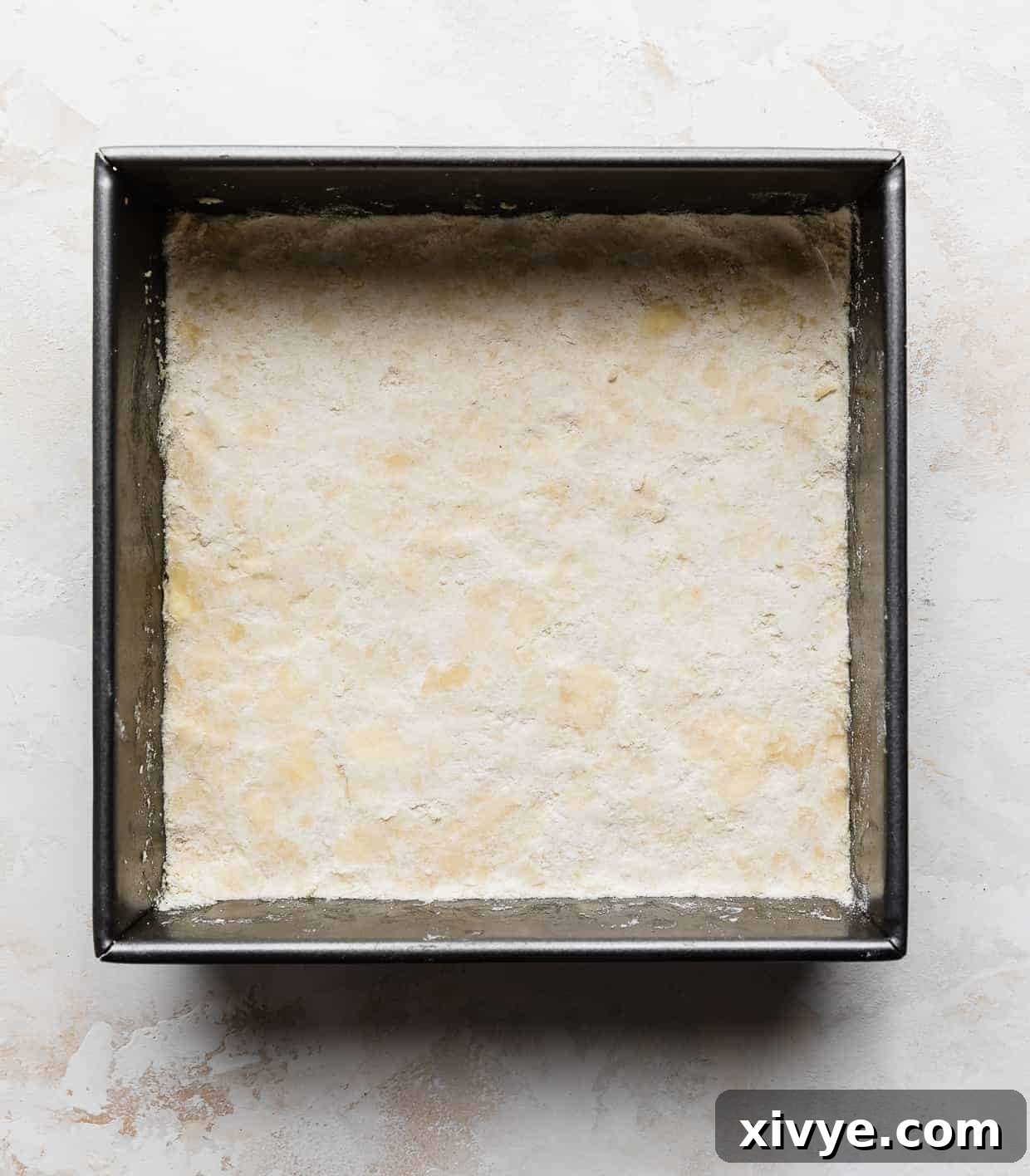 A square pan with a perfectly even layer of sweetened shortbread crust lining the bottom, golden and ready for the filling.