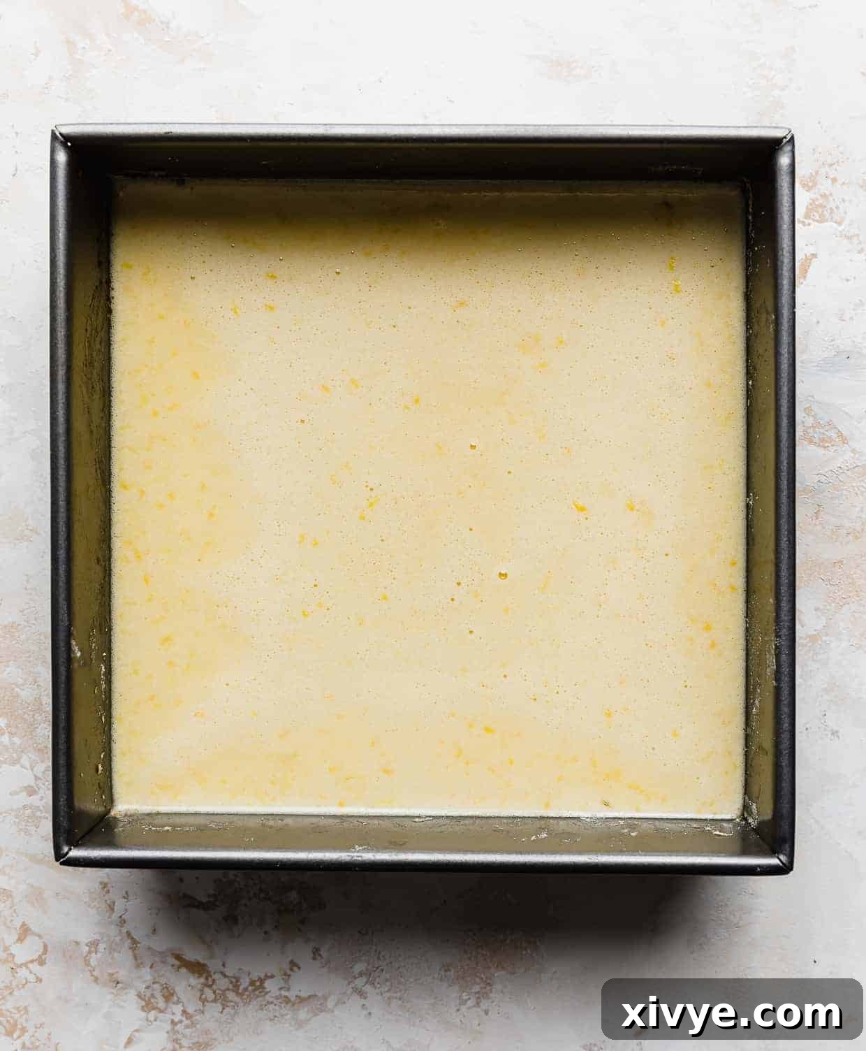 A square pan filled with the unbaked, bright yellow lemon bar filling, resting on the shortbread crust.