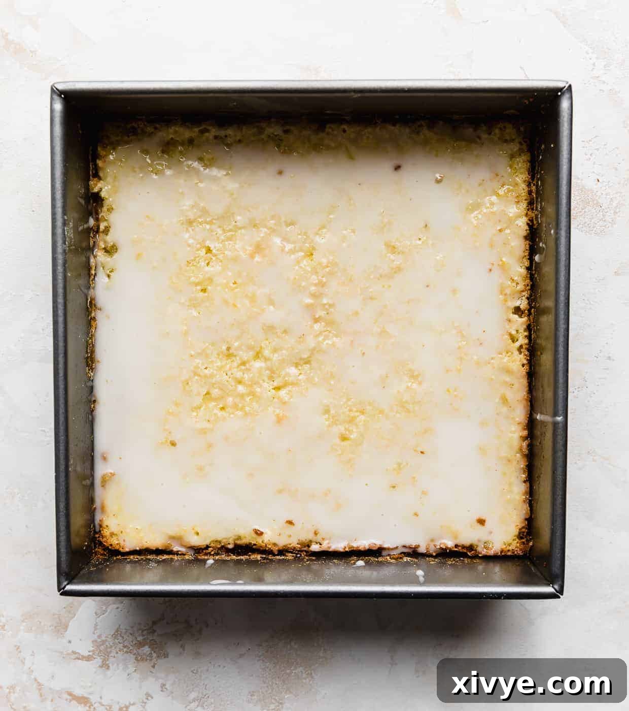 A square pan, resting on a white background, with baked lemon bars neatly arranged and glistening with a freshly drizzled glaze.
