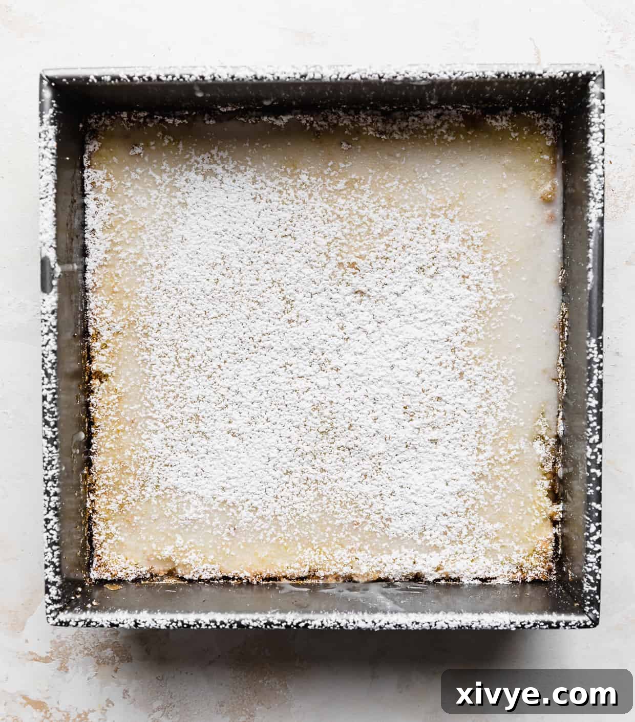 A square pan filled with a generous batch of lemon bars, beautifully topped with a delicate sprinkling of powdered sugar, inviting a taste.