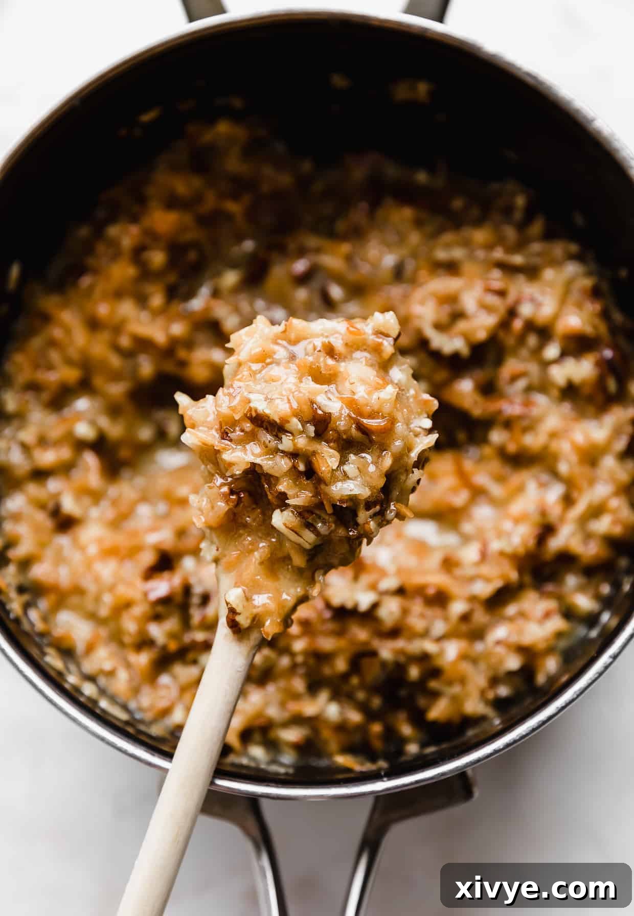 Decadent Coconut Pecan Dream 11 A wooden spoon full of coconut pecan frosting with the saucepan of the remaining frosting in the background.