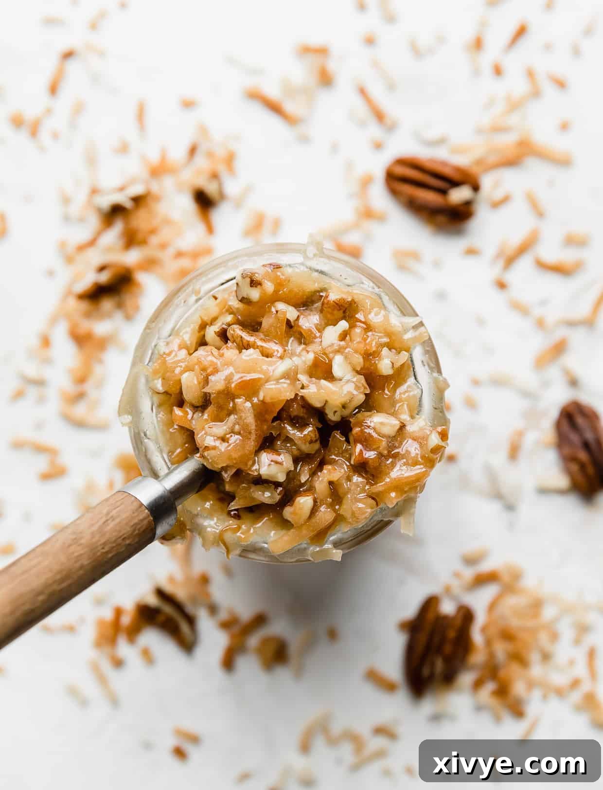 Decadent Coconut Pecan Dream 4 Overhead photo of German Chocolate Cake Frosting in a glass cup with toasted coconut and pecans around the perimeter of the cup.