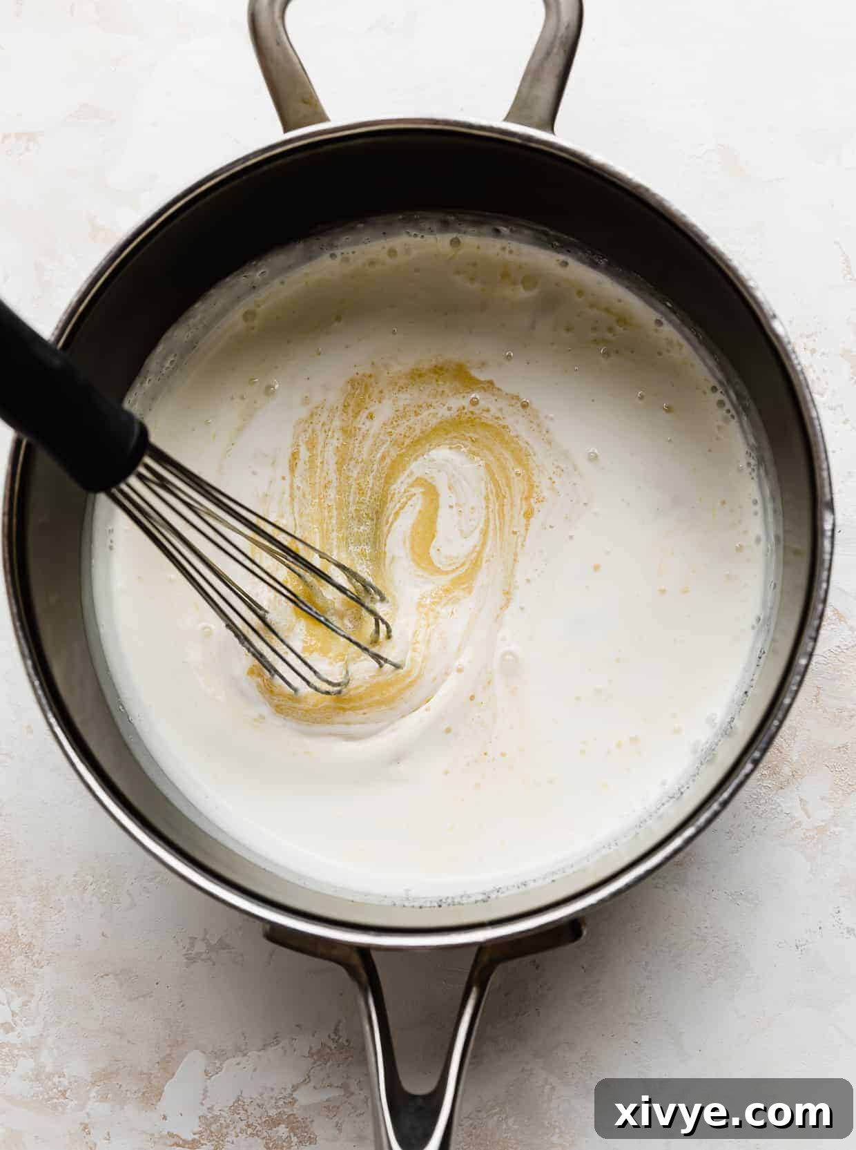 Decadent Coconut Pecan Dream 6 A whisk stirring the heavy cream, sugar, and egg yolks in a saucepan.