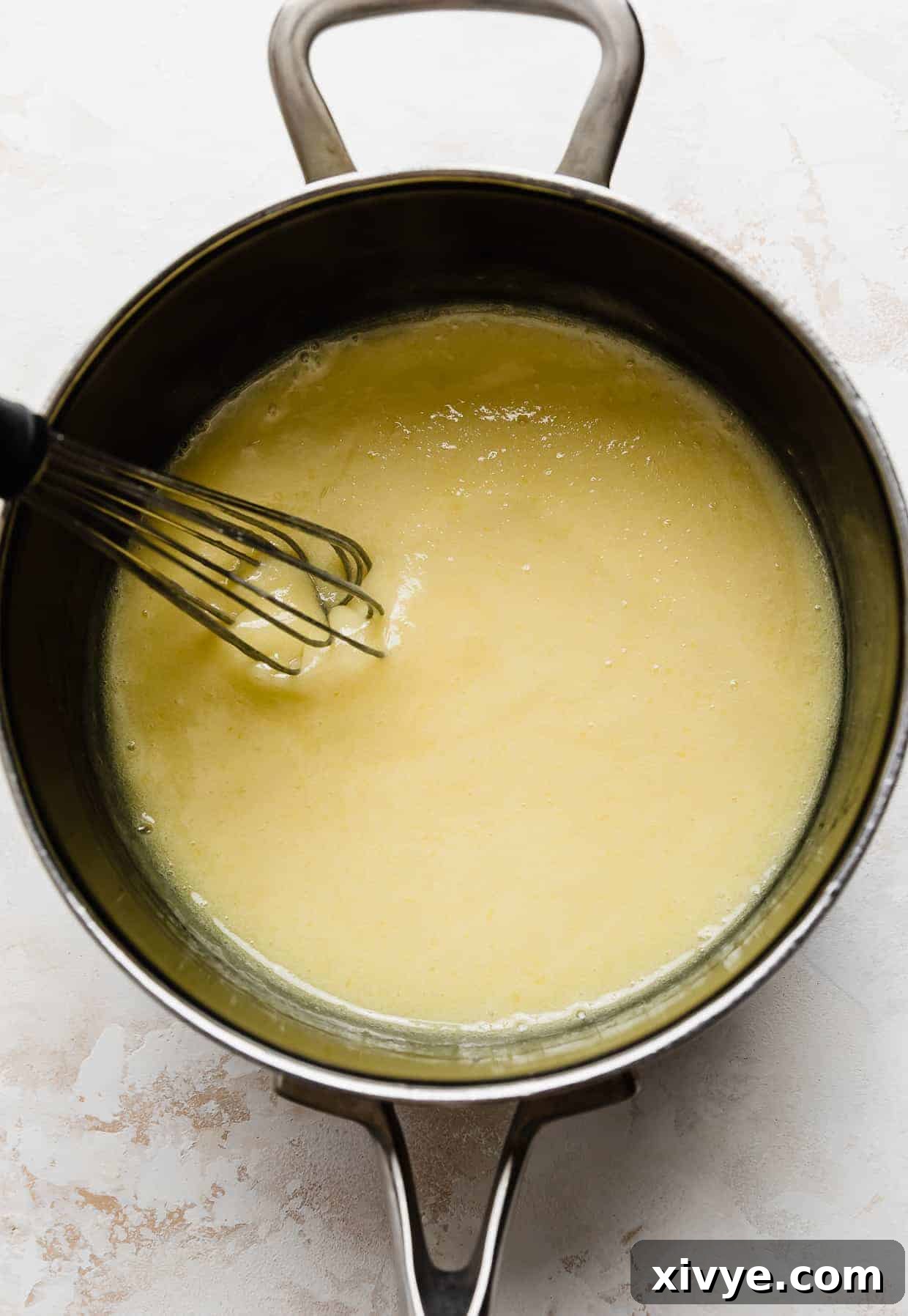 Decadent Coconut Pecan Dream 7 A saucepan with yellow thickened mixture in it, against a white background.