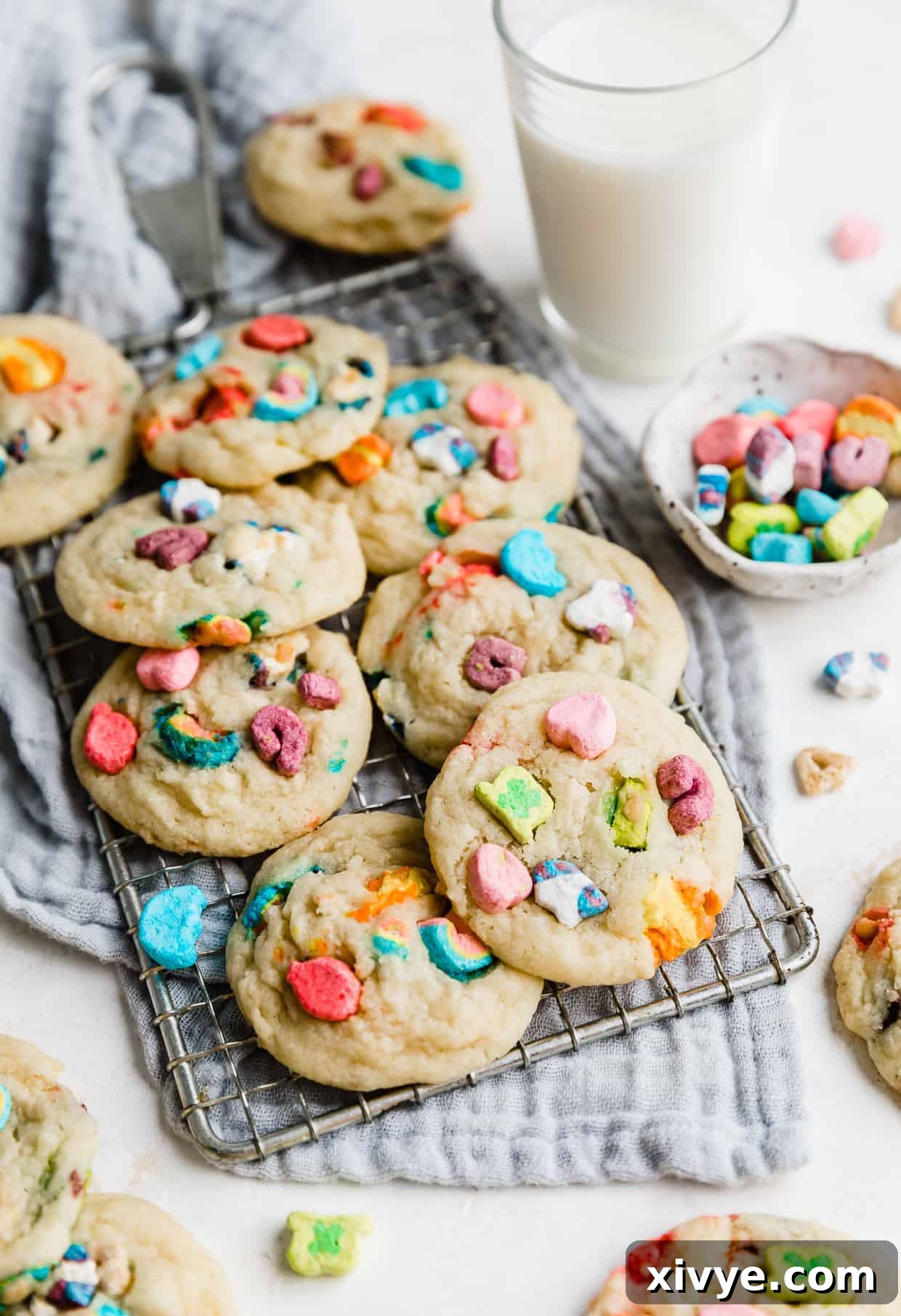 Several lucky charms marshmallow loaded sugar cookies on a wire rack against a gray napkin. 