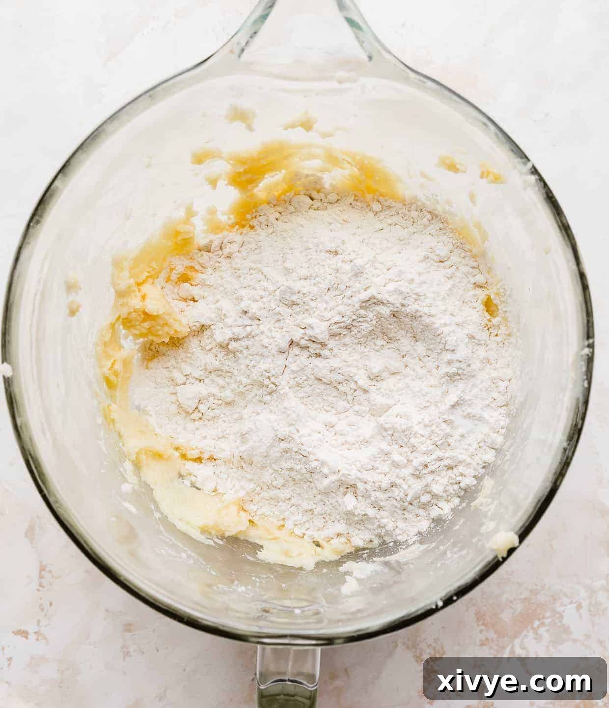 A glass mixing bowl with white flour overtop of the creamed butter and sugar.