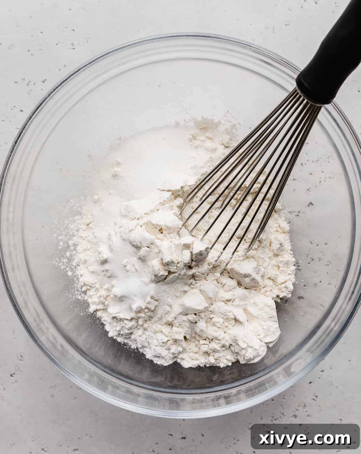 A glass bowl with a whisk and flour in it.