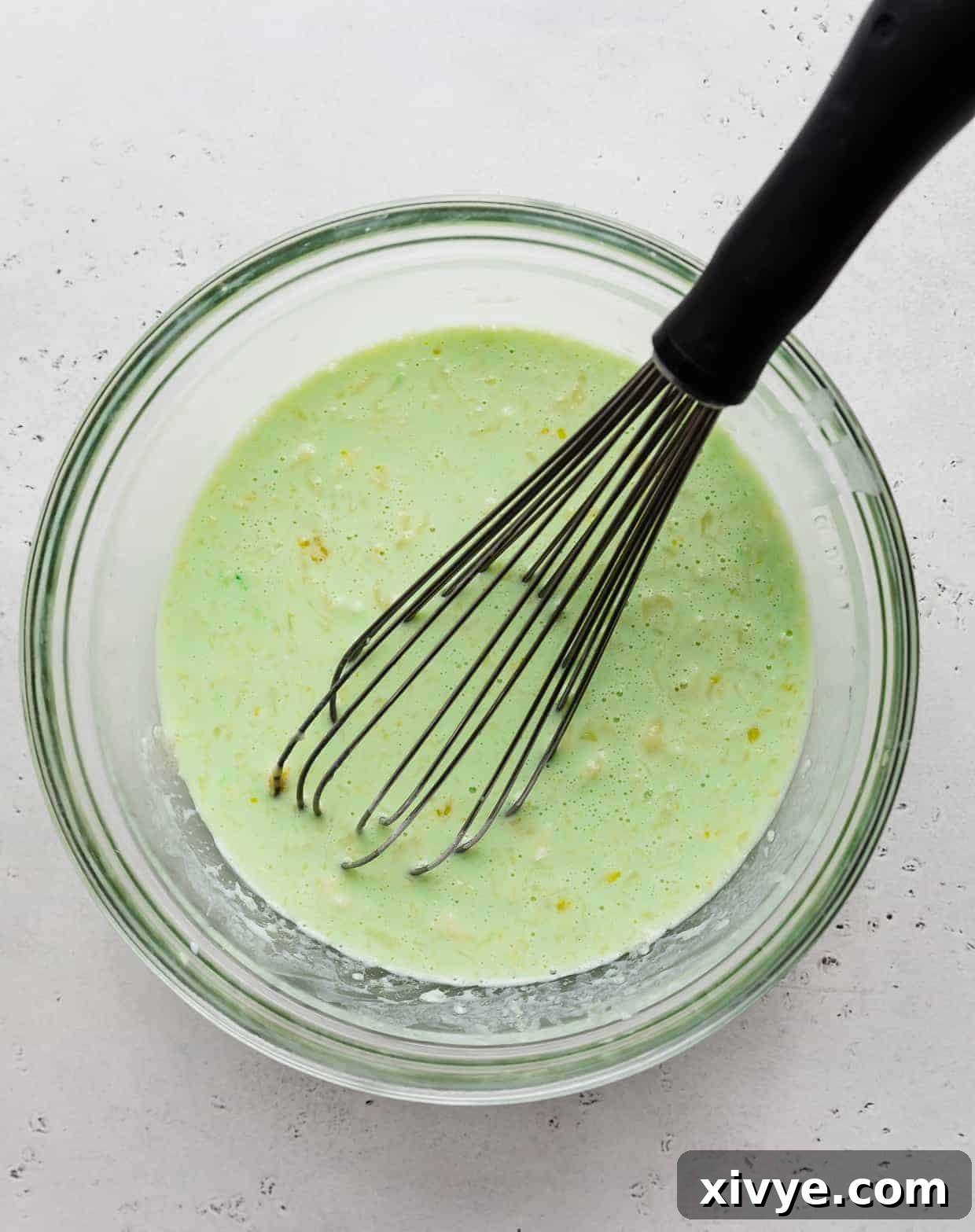 A green mixture in a glass bowl with a whisk in it. 