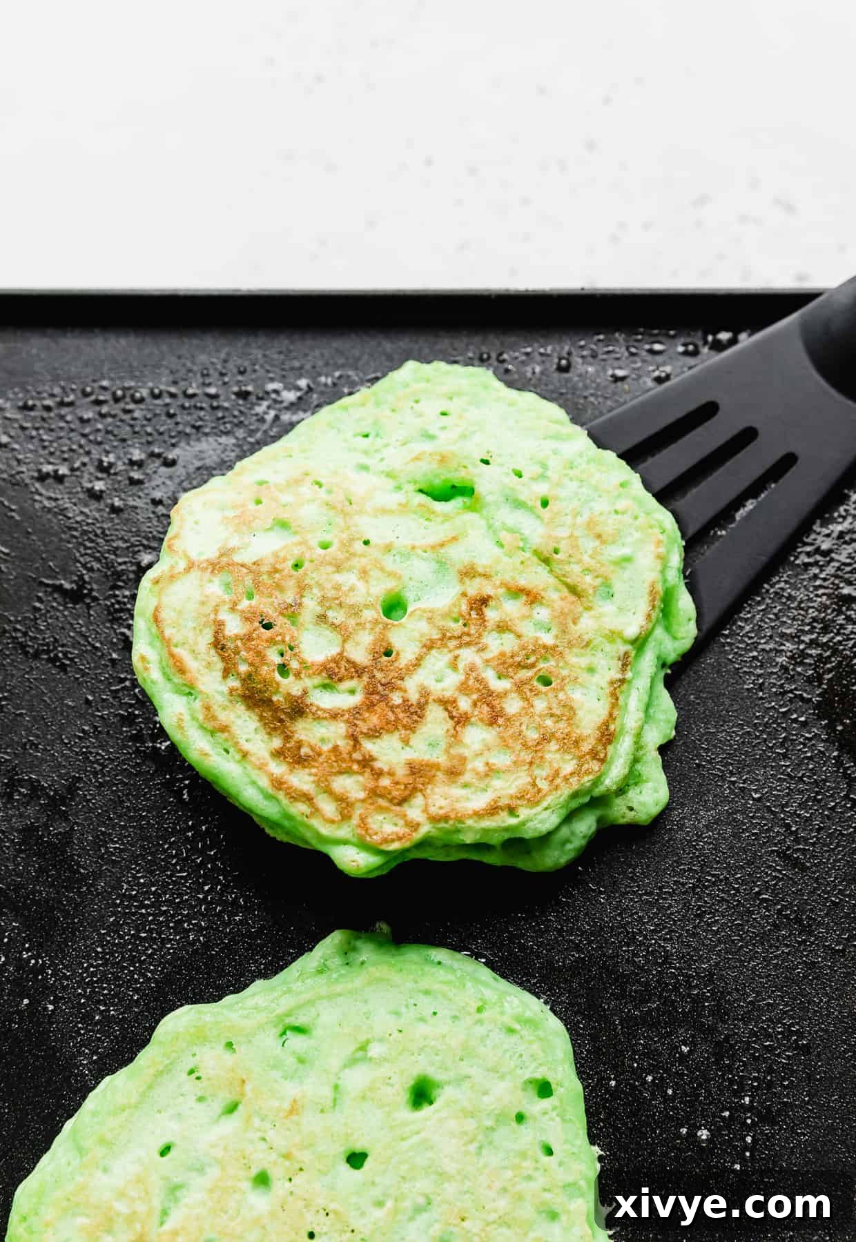 A green pancake on a black skillet with a black spatula underneath it. 