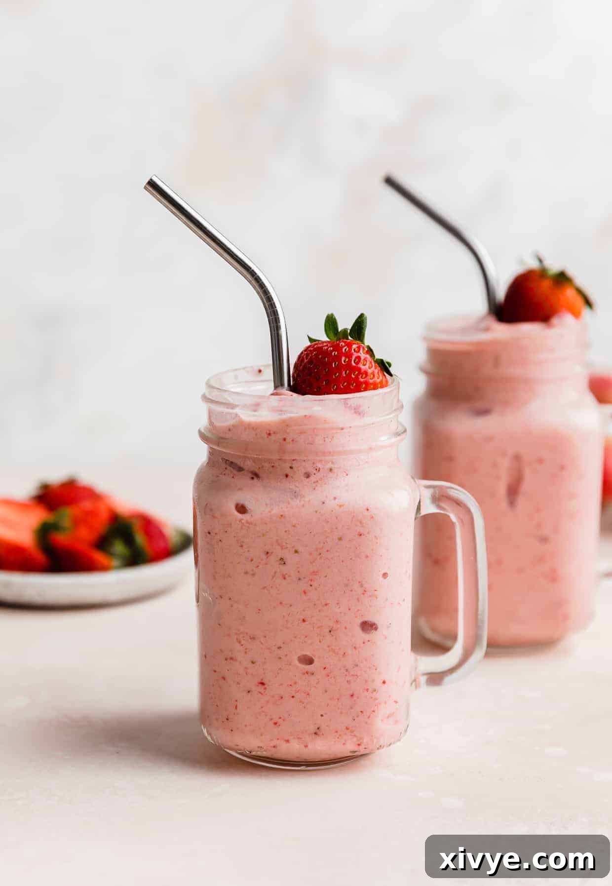Tropical Strawberry Pineapple Smoothie 2 Two mason jar glasses full of Strawberry Pineapple Smoothie with a fresh strawberry resting on the top of the smoothie.