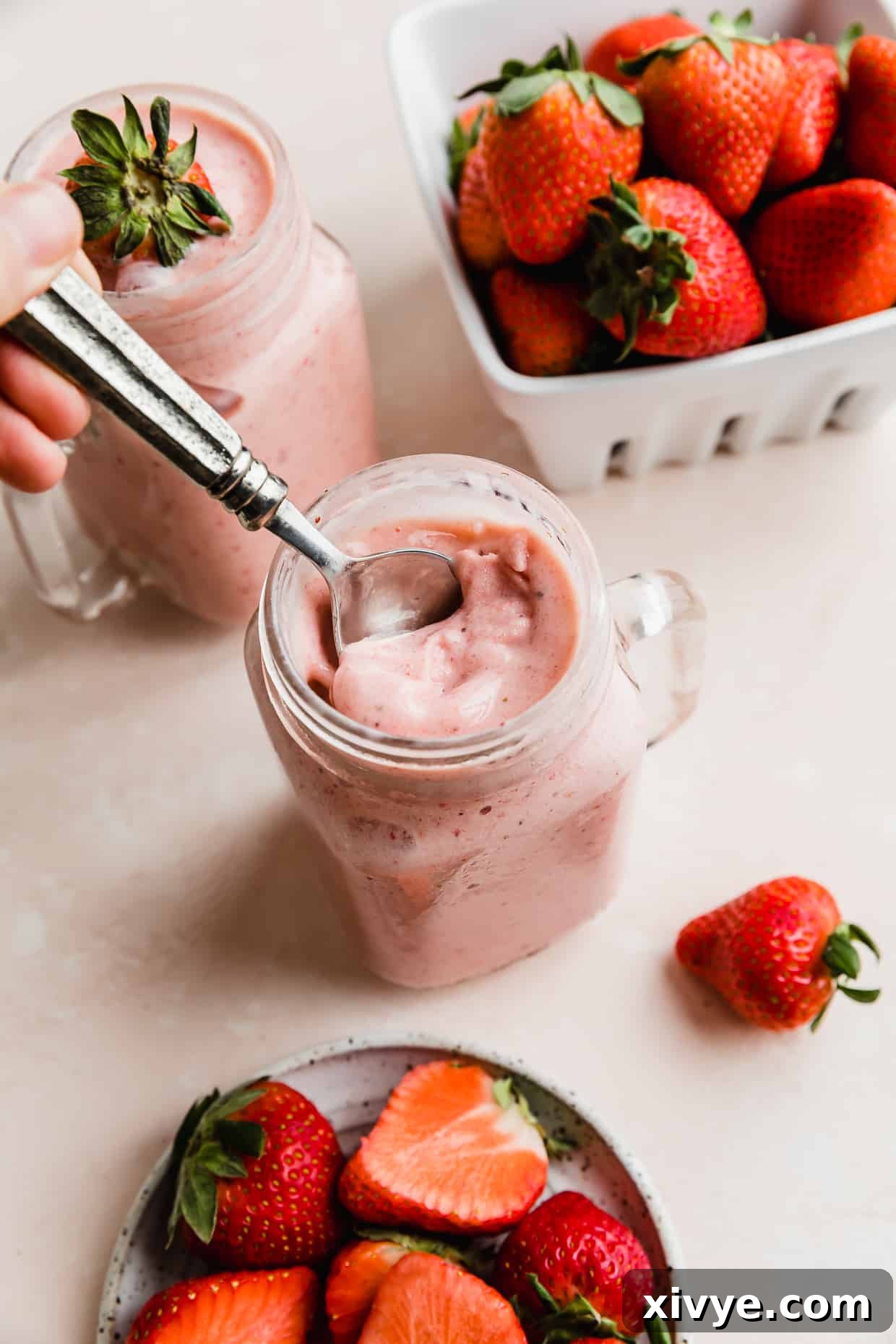 Tropical Strawberry Pineapple Smoothie 3 A spoon scooping up a portion of a strawberry pineapple smoothie that's in a mason glass jar, with a basket of strawberries in the background.